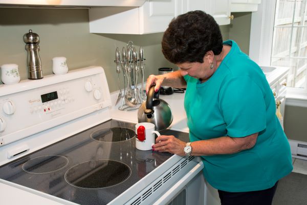 woman with vision loss pouring water from hot kettle in her kitchen 