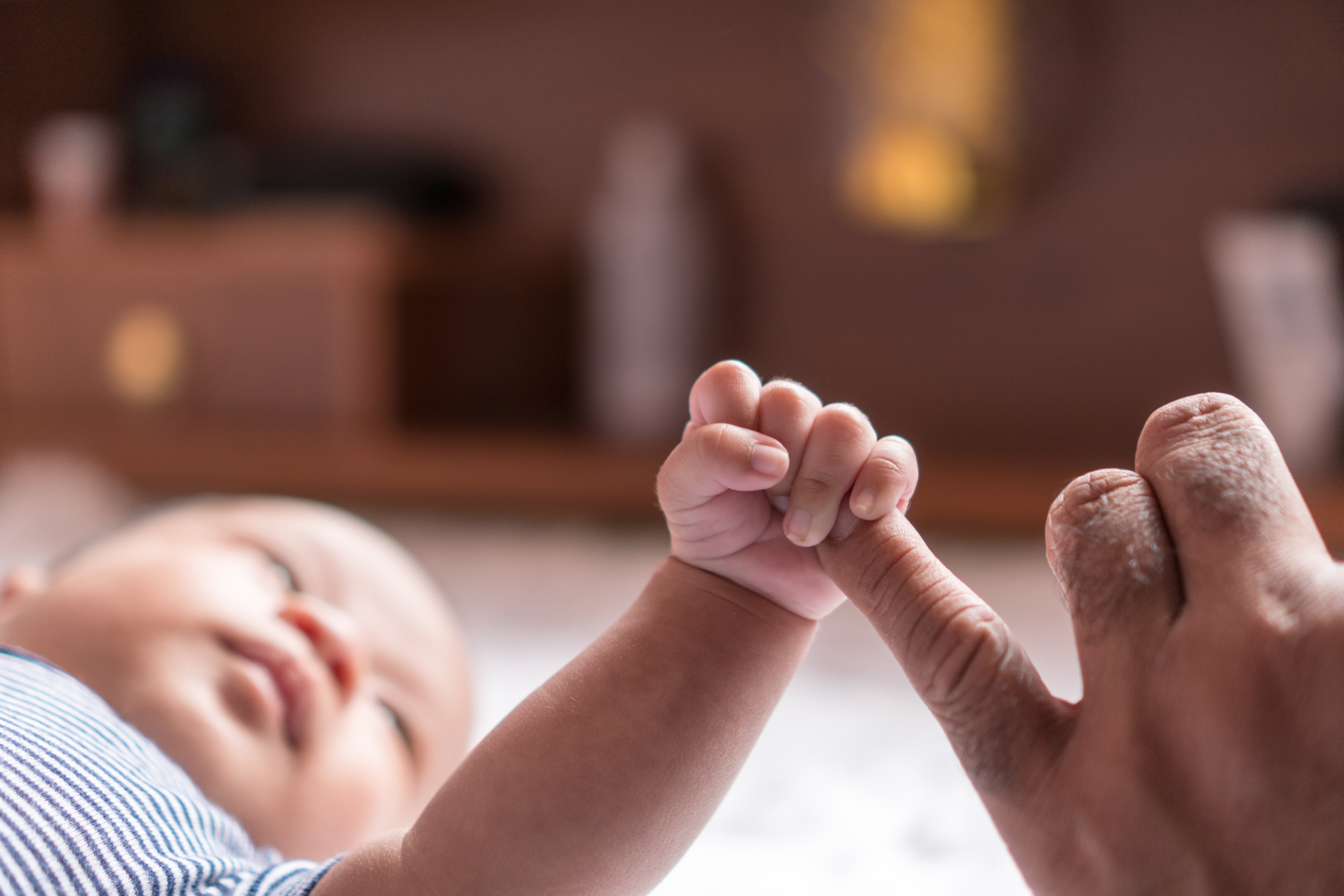 baby lying on floor grasps adults finger