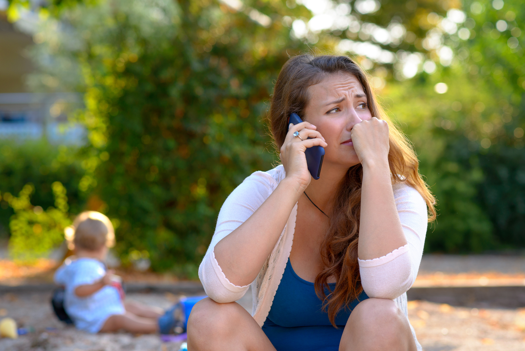 woman on phone, looks distressed. Child in background. 