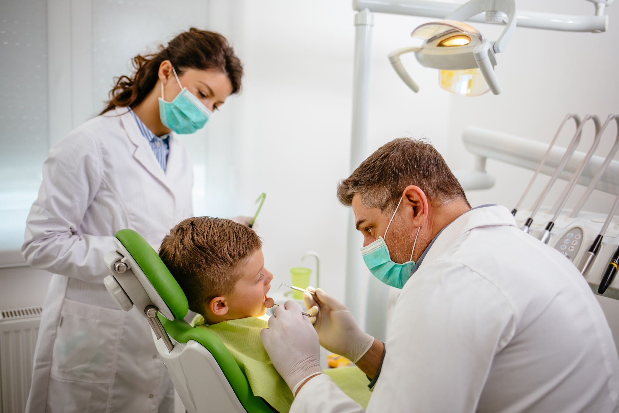 A male dentist is examining a child as a female assistant looks on. 