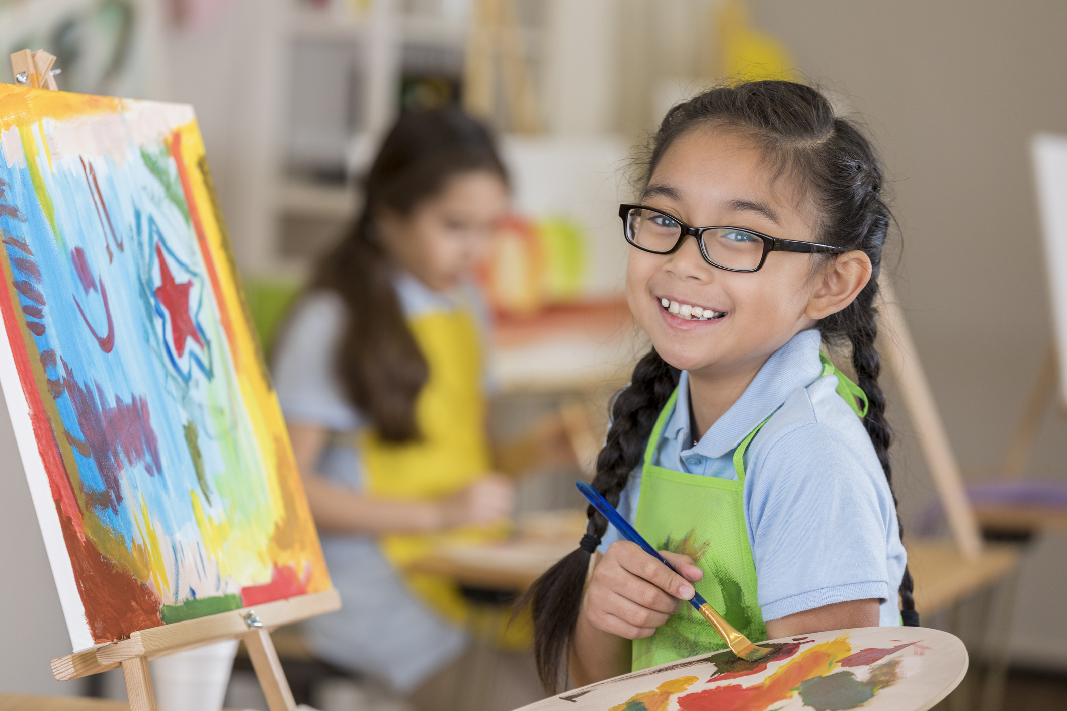 Young girl wearing glasses, painting, looks at camera