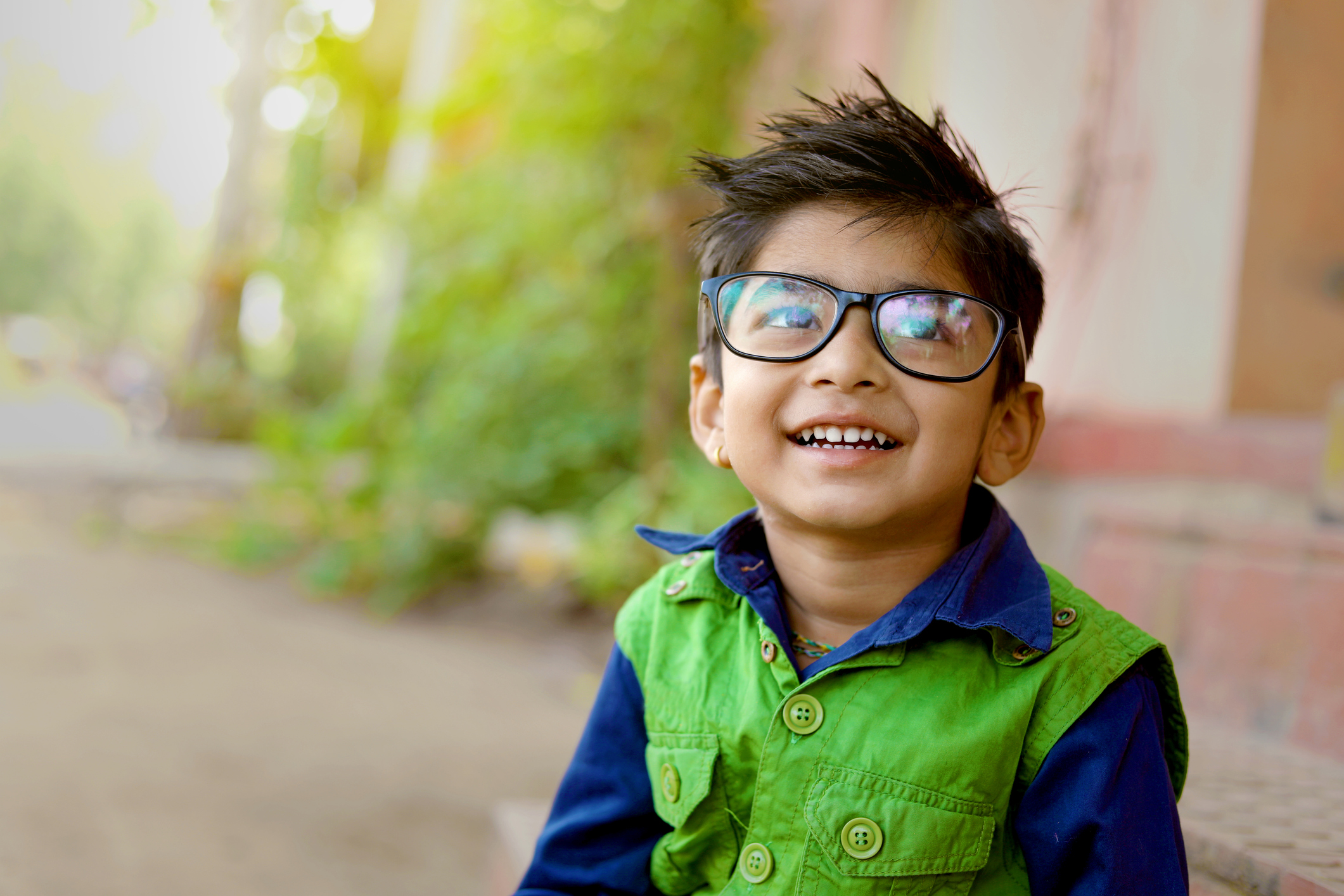 Young boy wearing a green vest and glasses smiles at the camera. 
