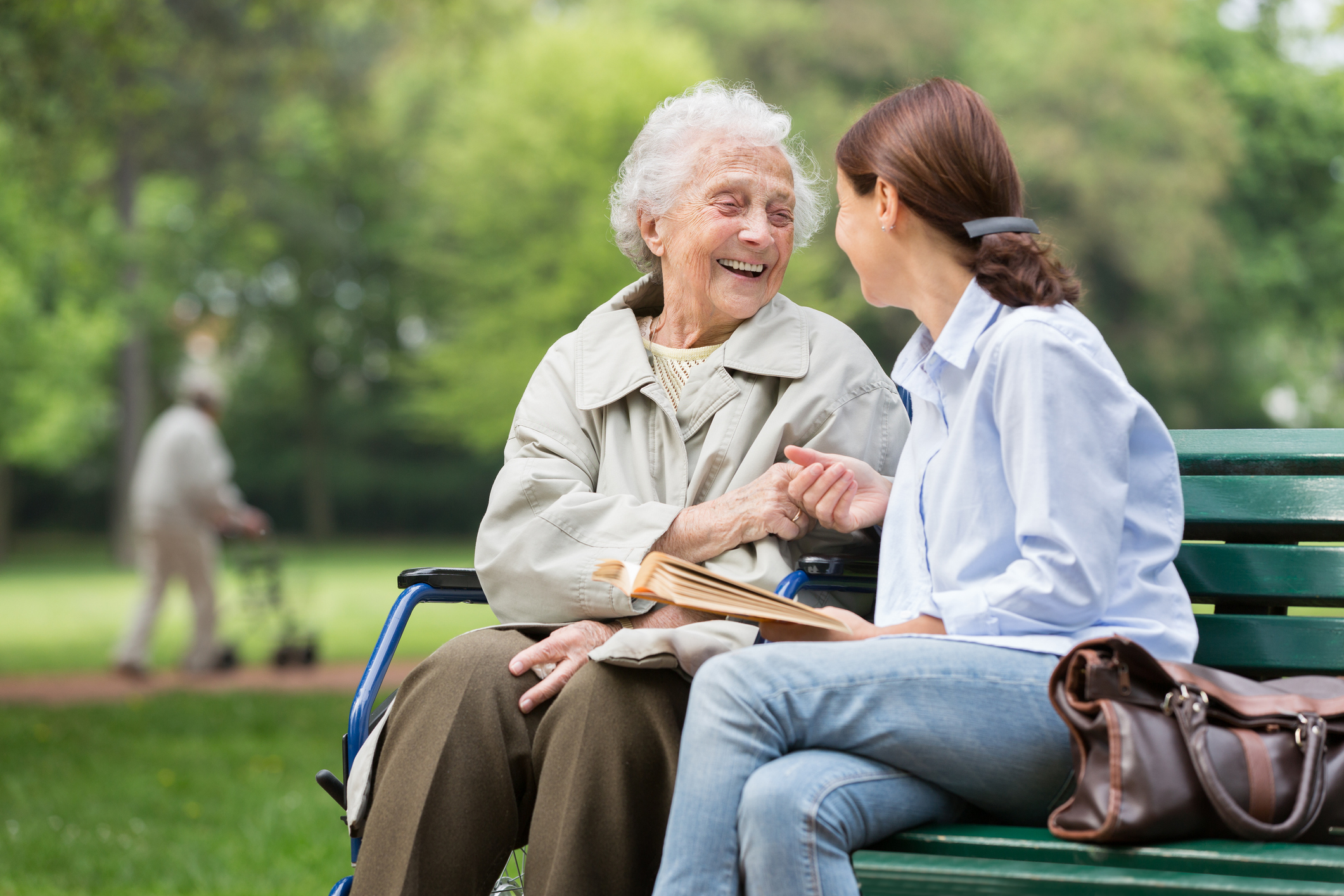 caregiver sitting with elderly loved one on a park bench