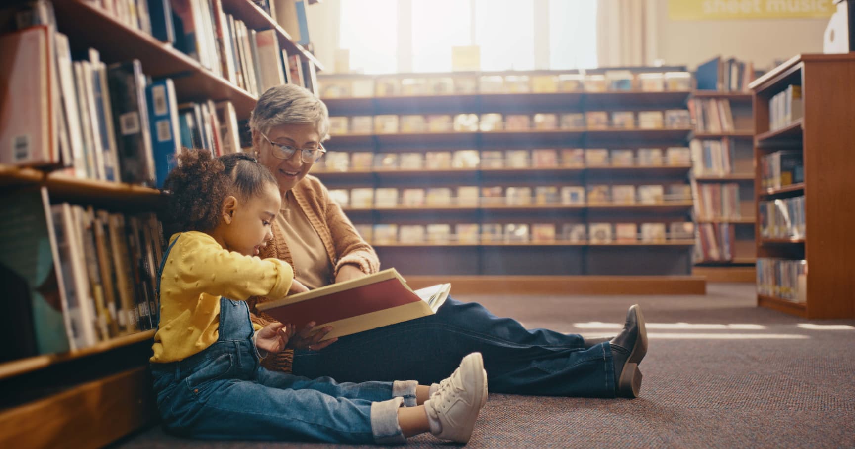 Grandmother reading book with granddaughter at the library.