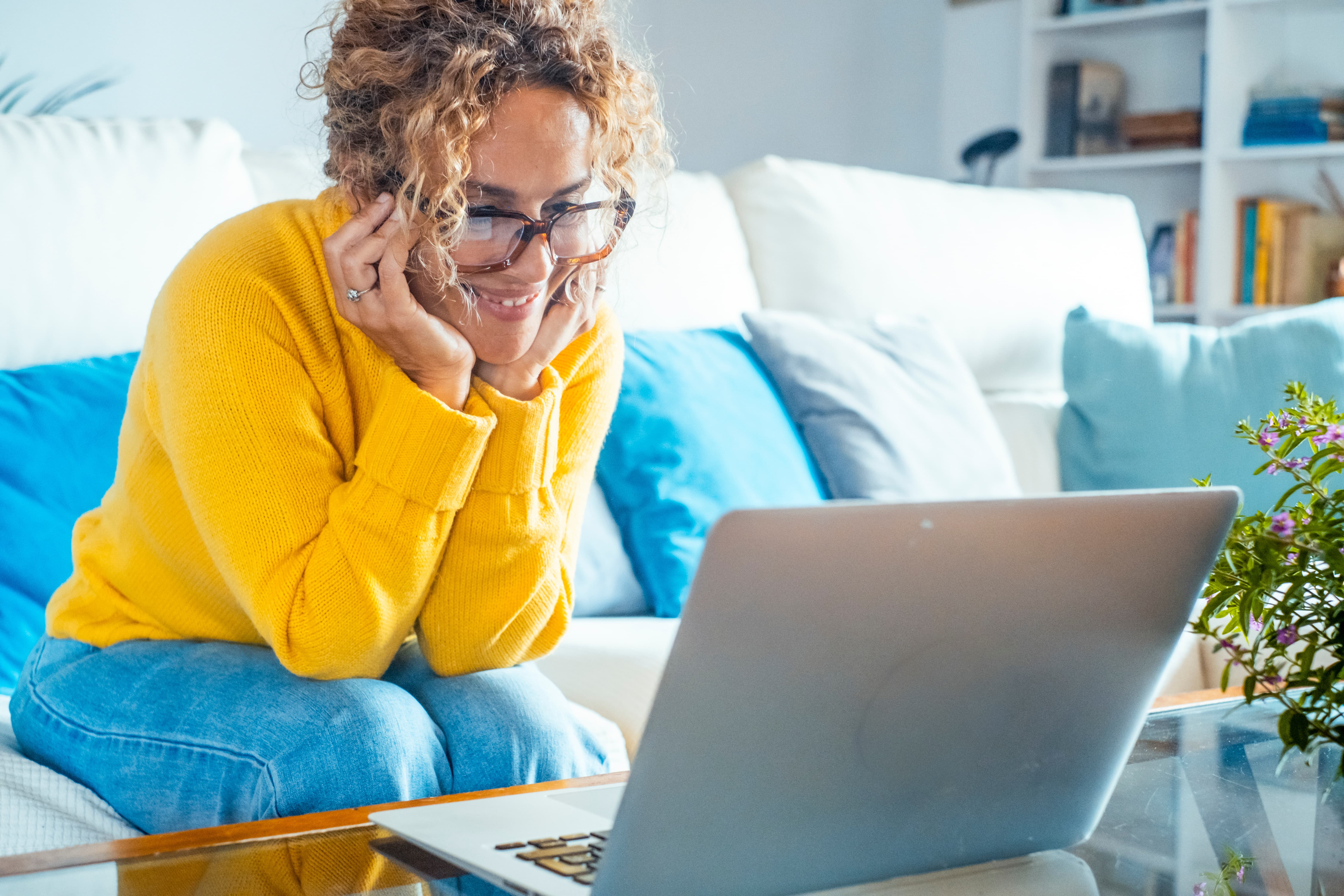 Person sitting on couch smiling while using laptop.