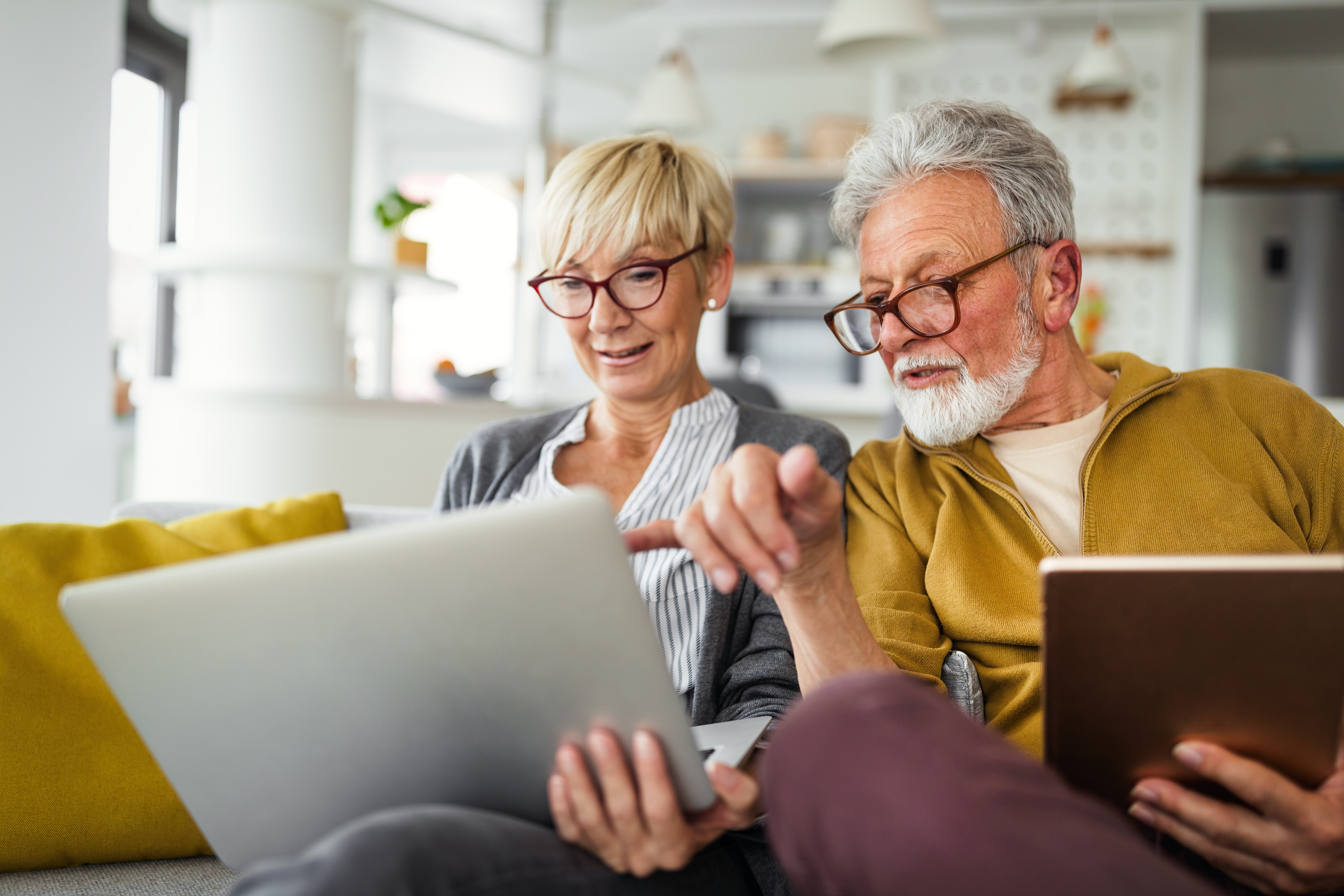 Senior couple sitting on sofa using laptop together